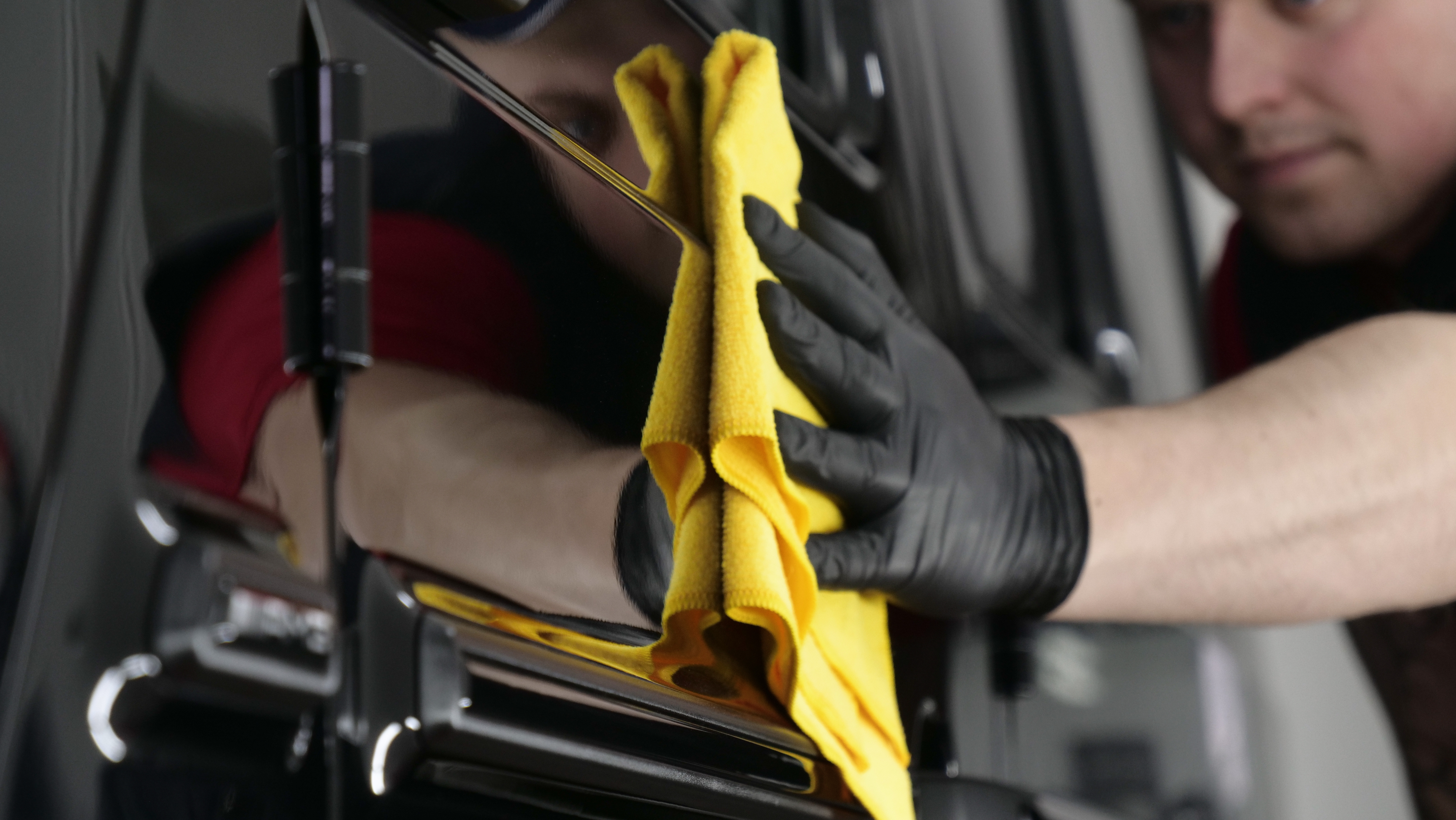 Technician in black gloves cleaning car window with yellow microfiber cloth
