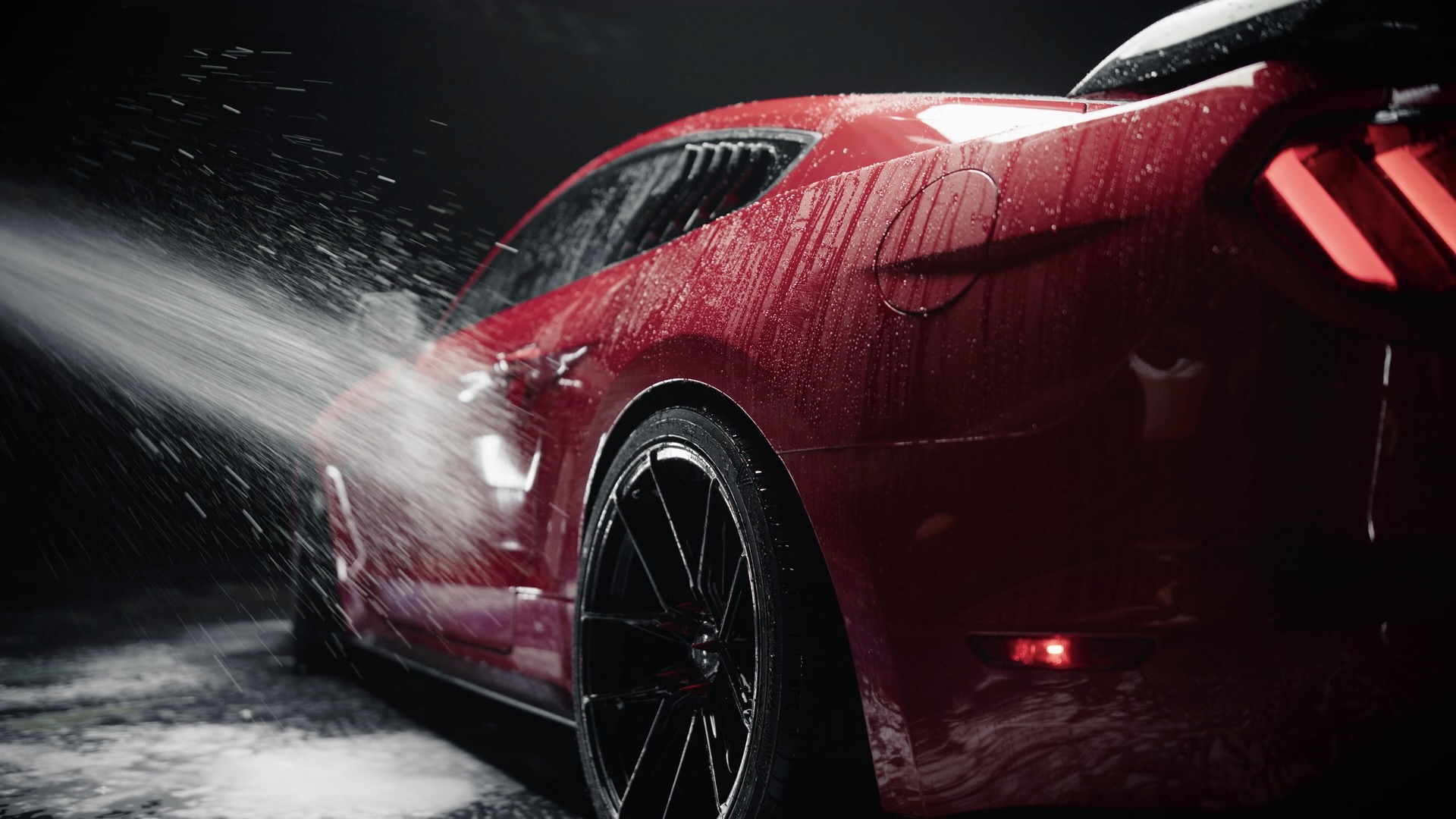 Red car being washed with high pressure water spray against dark background