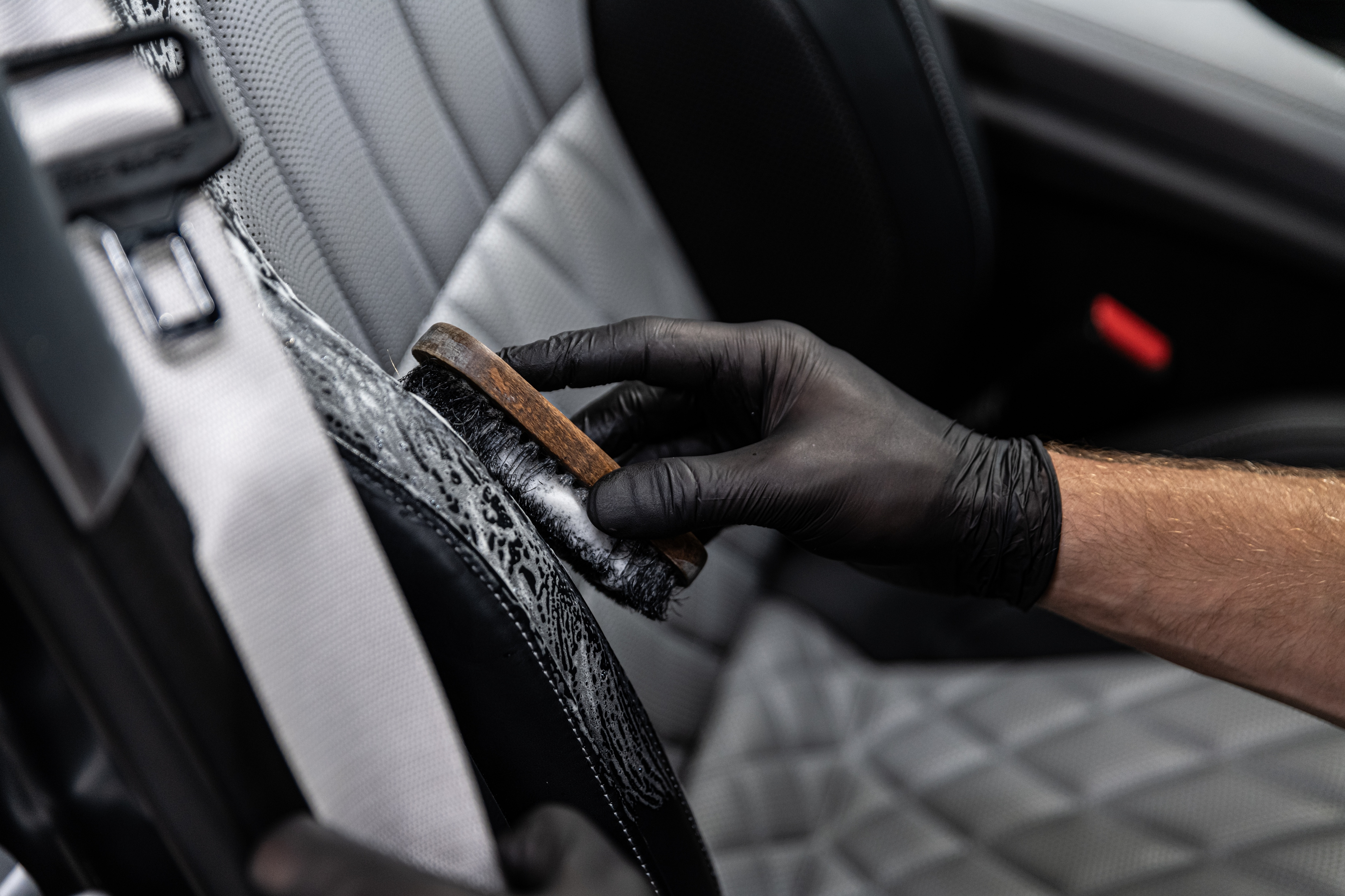 Professional detailing a car seat with a brush while wearing black gloves