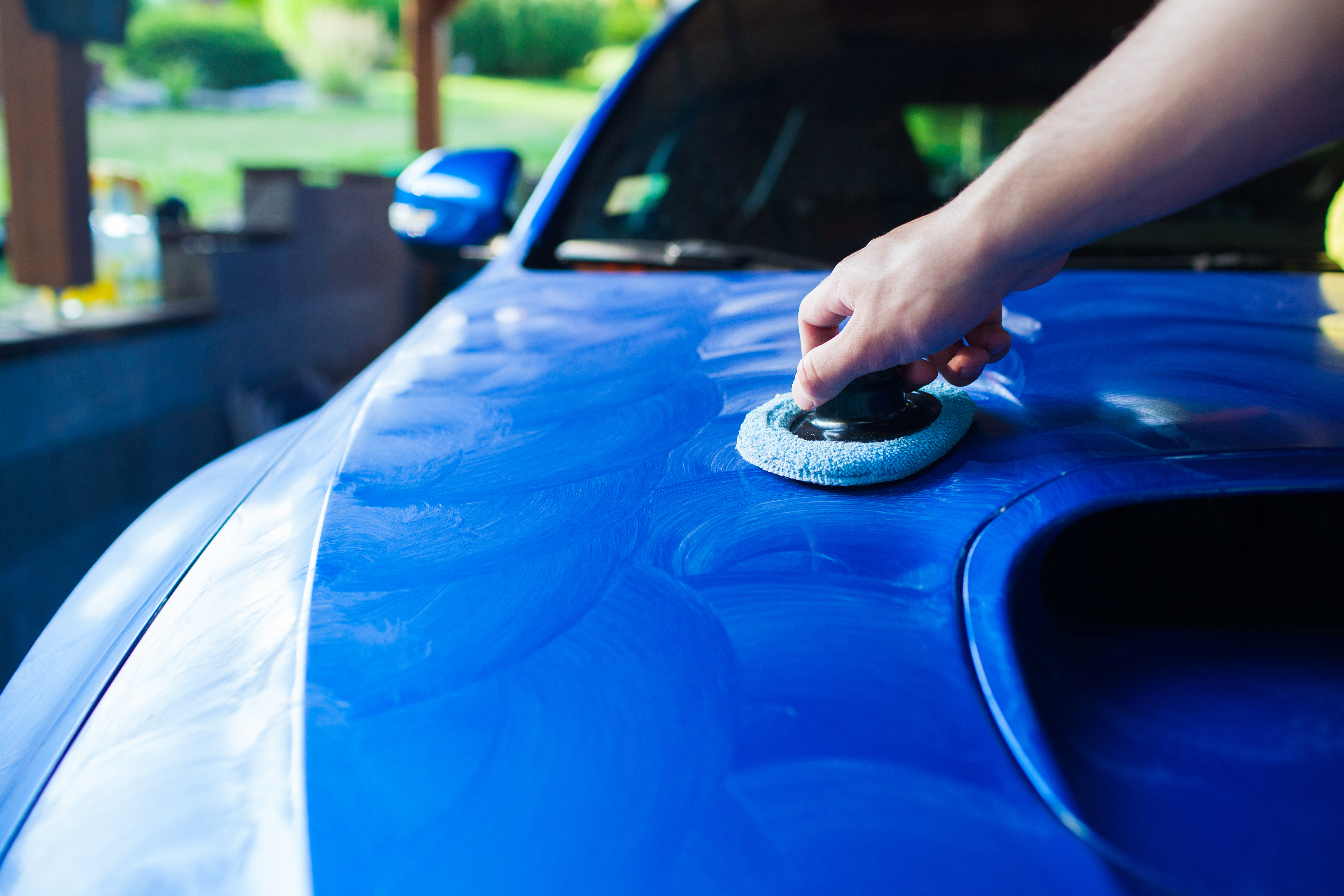 Person polishing blue car hood with round buffing pad outdoors